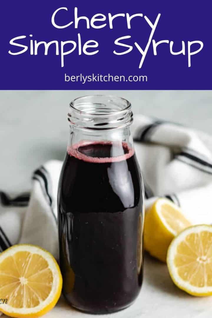 Cherry simple syrup in a bottle surrounded by halved lemons.