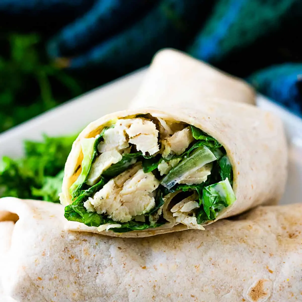 Chicken Caesar wraps stacked on each other on a white plate.