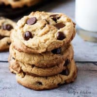 Stack of peanut butter cookies with chocolate chips in front of a cup of milk.