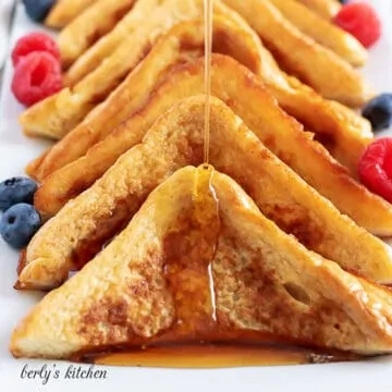 Several pieces of French toast on a platter being drizzled with syrup.