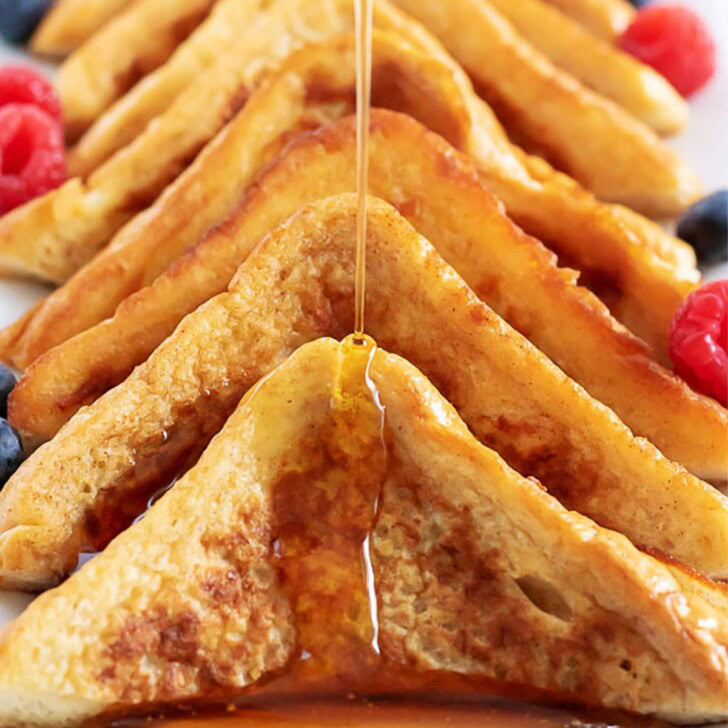 Several pieces of French toast on a platter being drizzled with syrup.