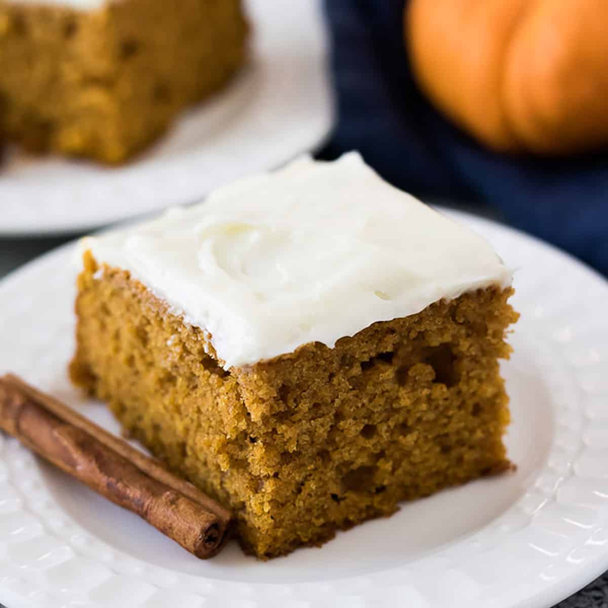 Slice of pumpkin cake with frosting on a white plate.