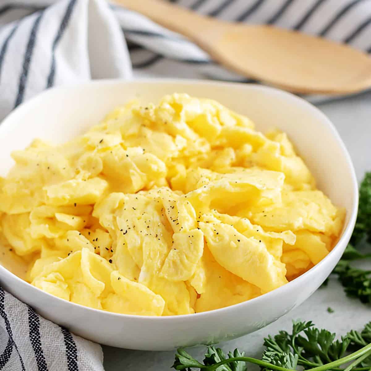 Fluffy scrambled eggs sprinkled with pepper in a white bowl.