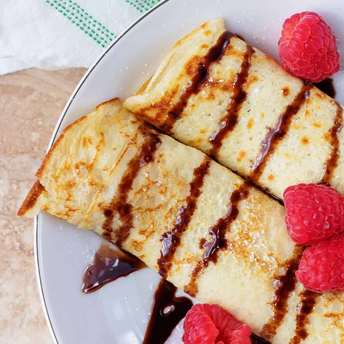 Crepes drizzled with chocolate sauce and topped with fresh raspberries.
