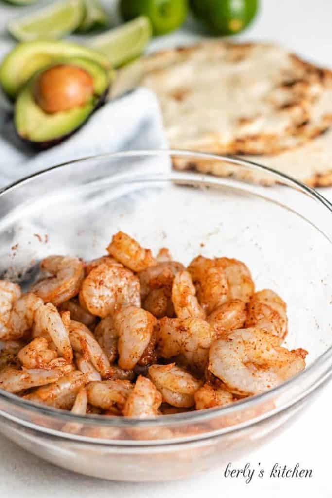 Raw shrimp in a mixing bowl sprinkled with spices.