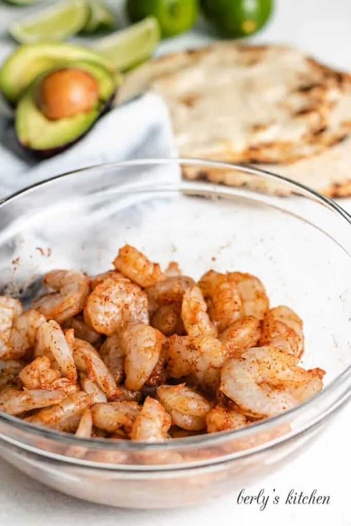Raw shrimp in a mixing bowl sprinkled with spices.