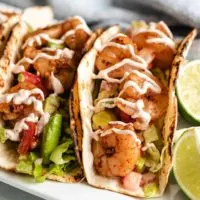 Two grilled shrimp tacos drizzled with chipotle sauce.