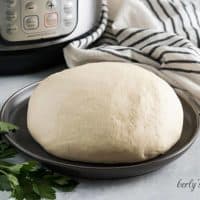 Gray plate of pizza dough in front of a black and white towel.