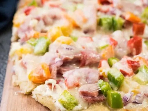 Leftover ham and veggie flatbread pizza on a cutting board.