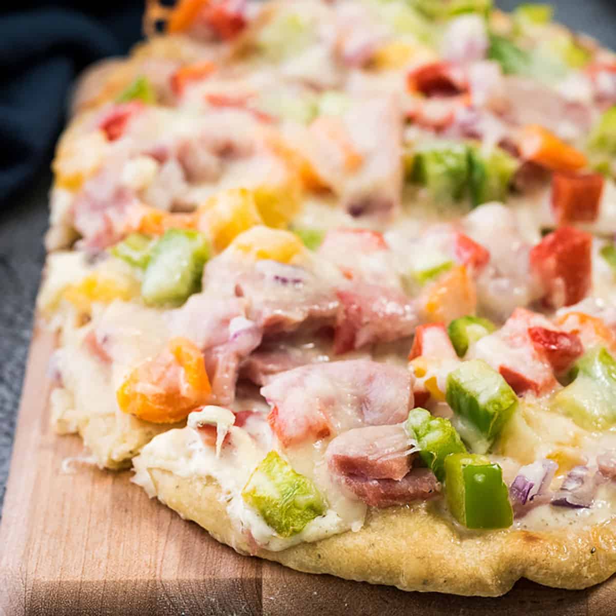 Leftover ham and veggie flatbread pizza on a cutting board.