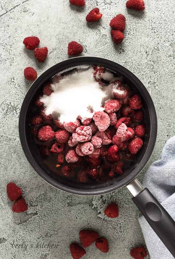 Frozen raspberries, sugar, and water in a saucepan.
