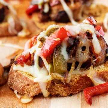 Sausage and peppers crostini on a cutting board.