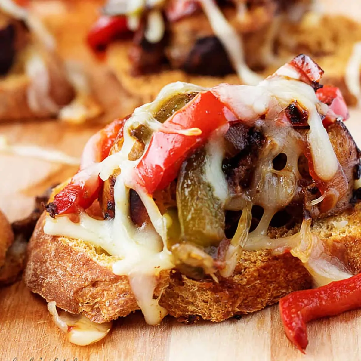 Sausage and peppers crostini on a cutting board.