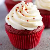 A red velvet cupcake in a red cupcake liner with cream cheese frosting.