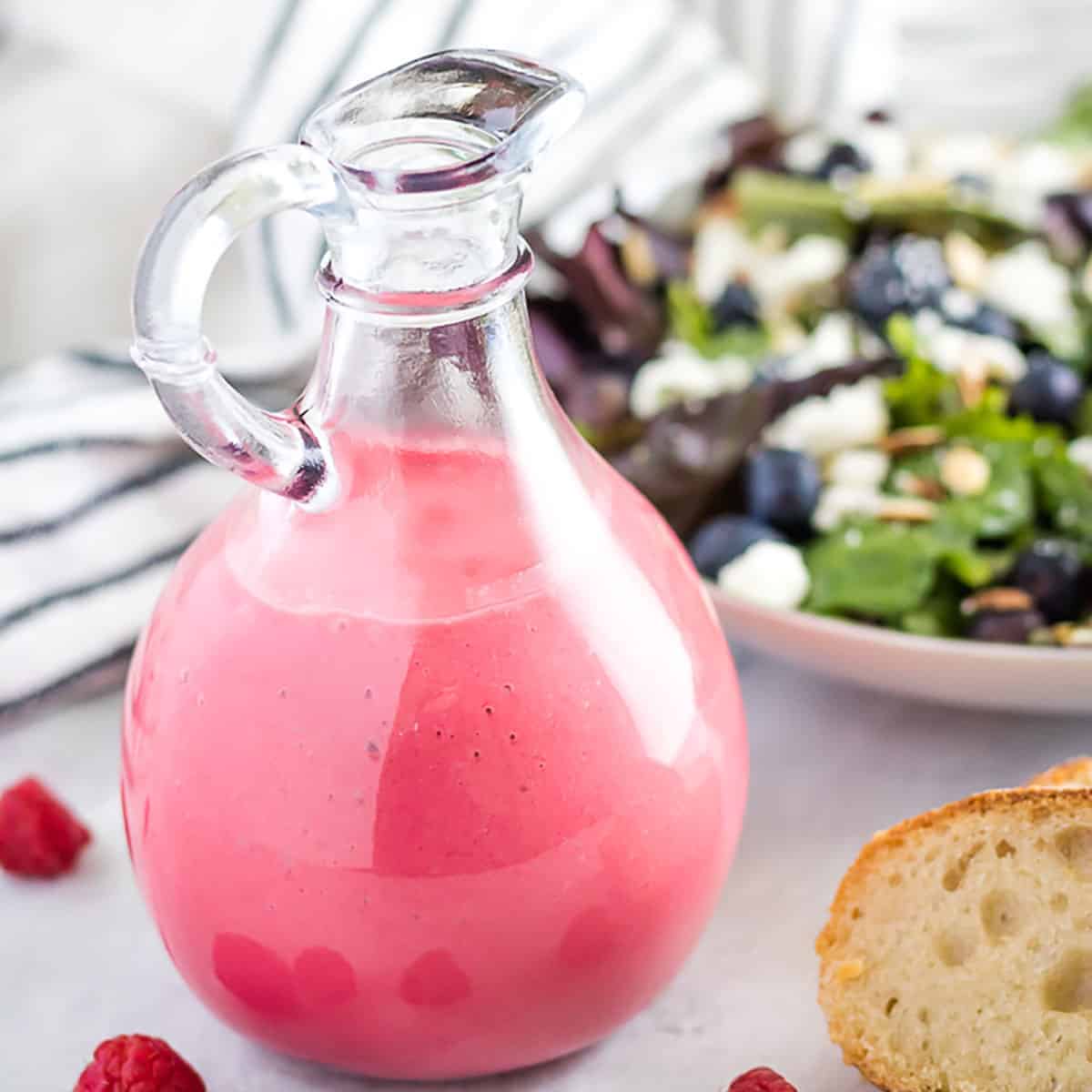 A jar of raspberry vinaigrette dressing with fresh raspberries and a salad.