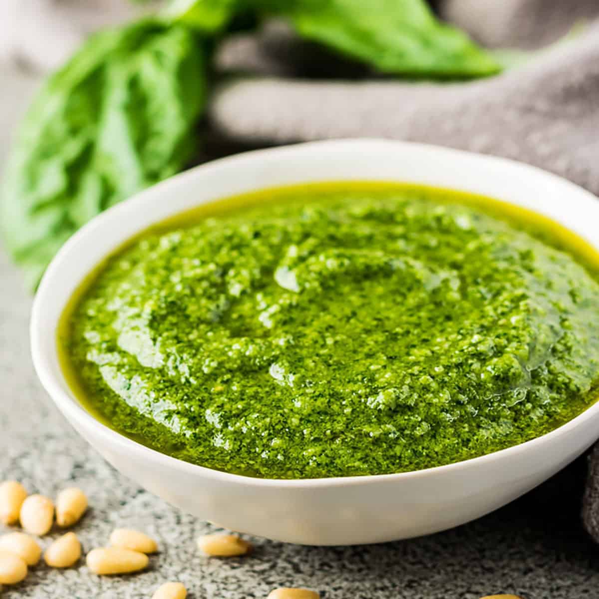 Creamy pesto sauce in a small bowl next to pine nuts.
