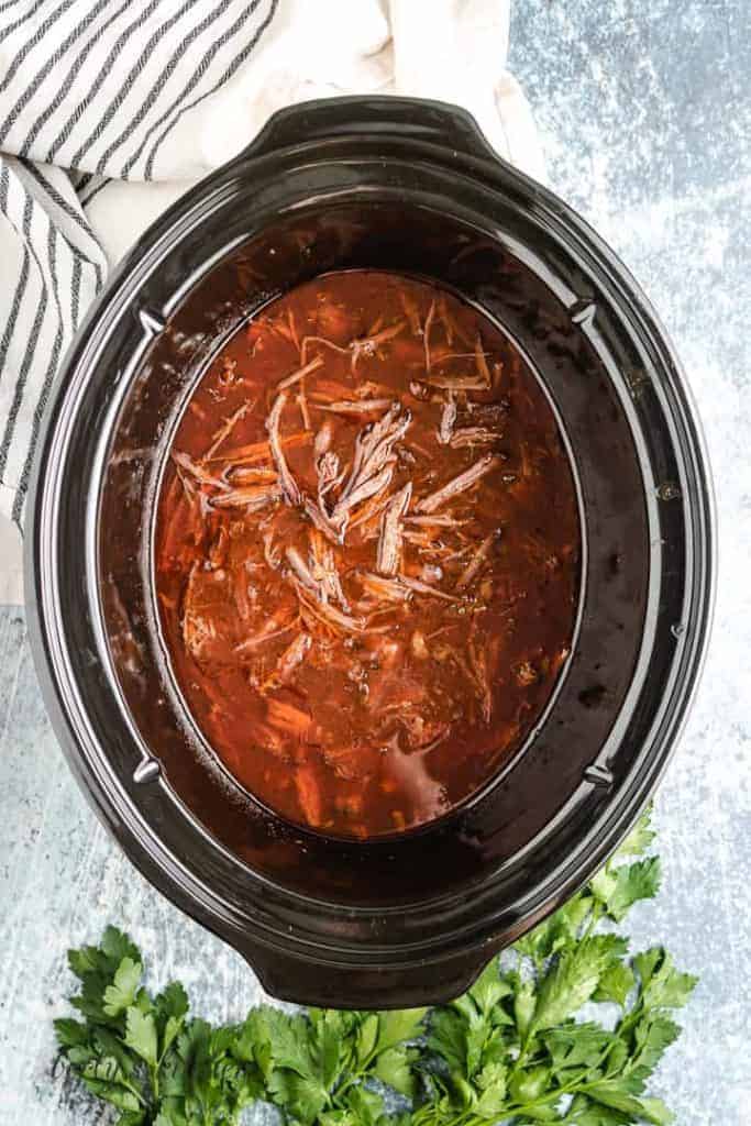 The beef has been shredded and returned to the crock pot.