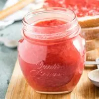 Jar of homemade strawberry jam sitting on a cutting board.