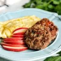 A blue plate with the cooked sausage, sliced apples, and scrambled eggs.