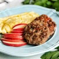 Two cooked turkey sausage patties served with sliced apples and scrambled eggs.