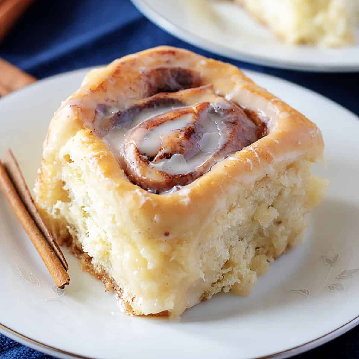 Homemade cinnamon roll on a plate with a cinnamon stick.