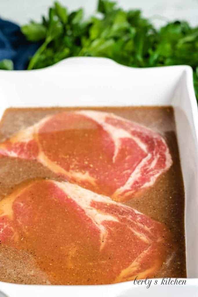 Two steaks marinated in a baking dish.