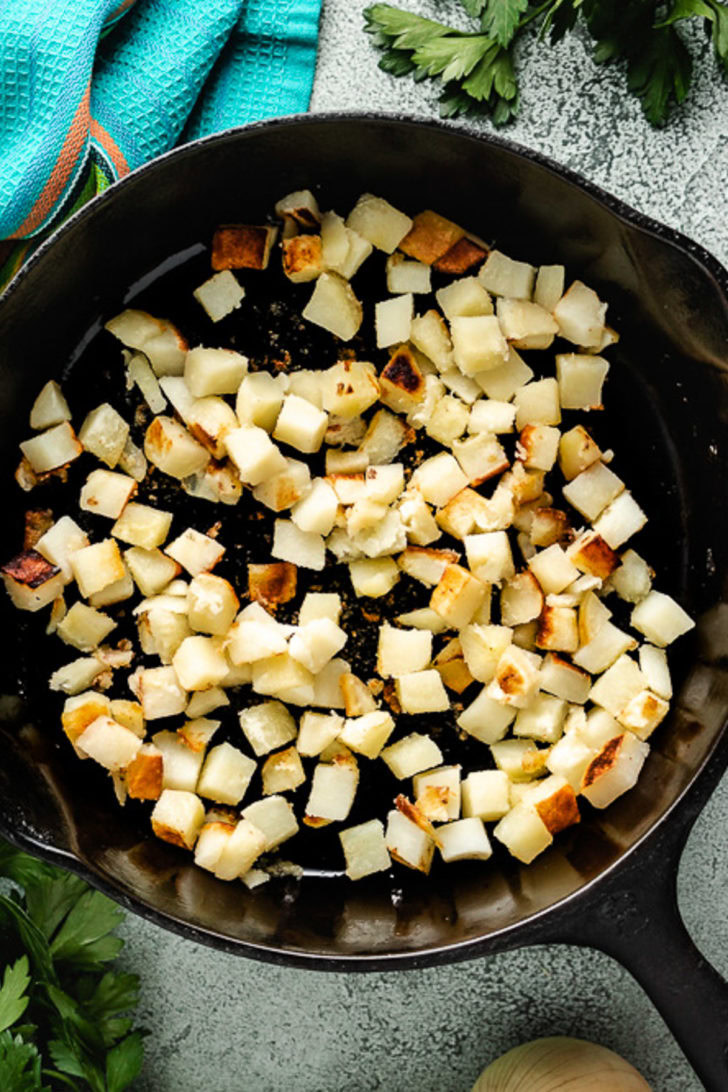 Diced potatoes cooking in a cast iron skillet.