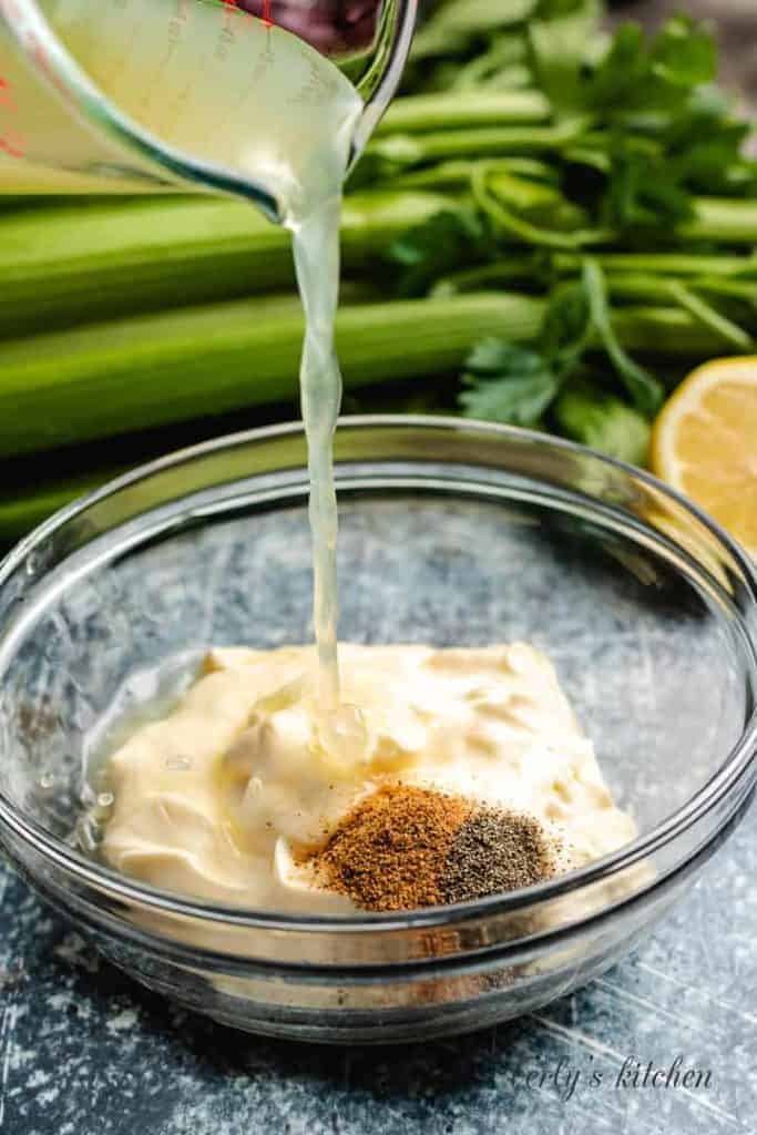 Lemon juice being poured into a bowl with dressing ingredients.