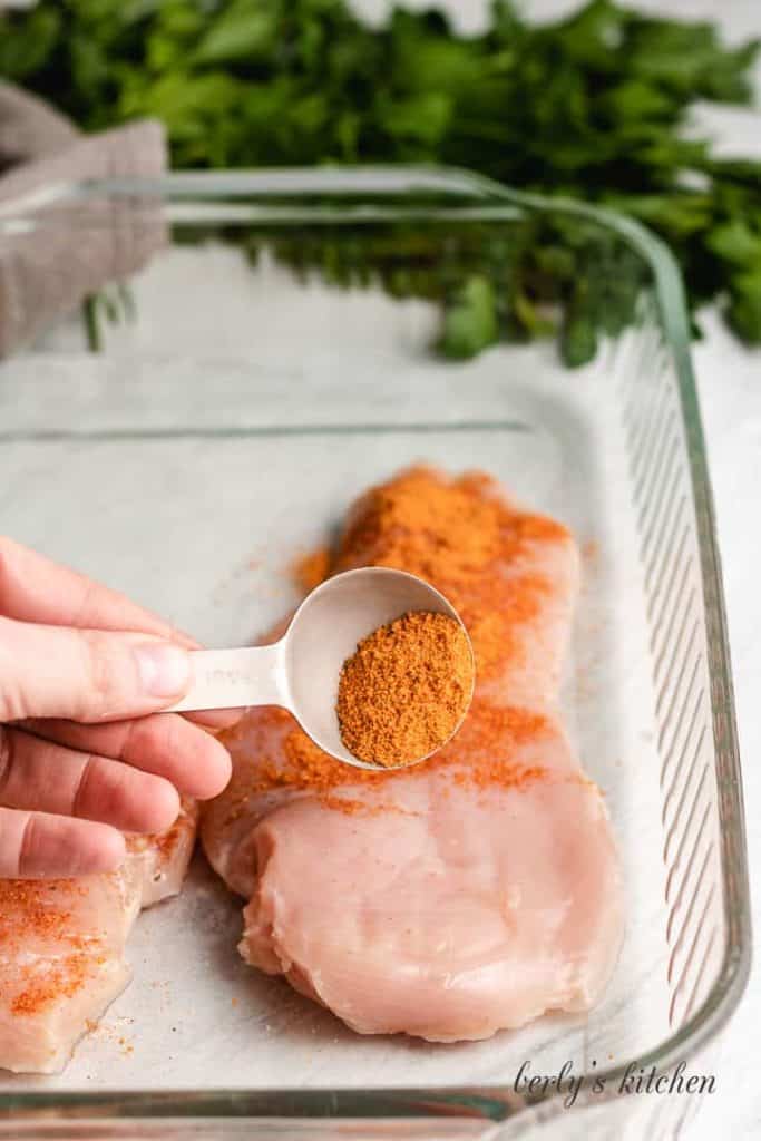 Bbq rub being sprinkled over the raw chicken.