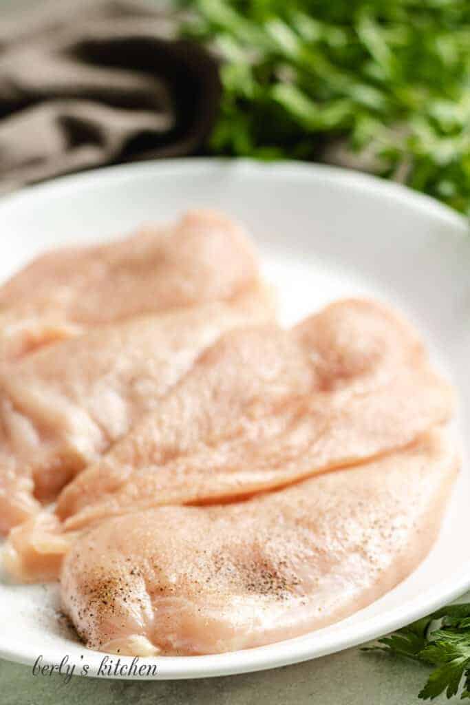 Raw seasoned chicken breast on a plate.