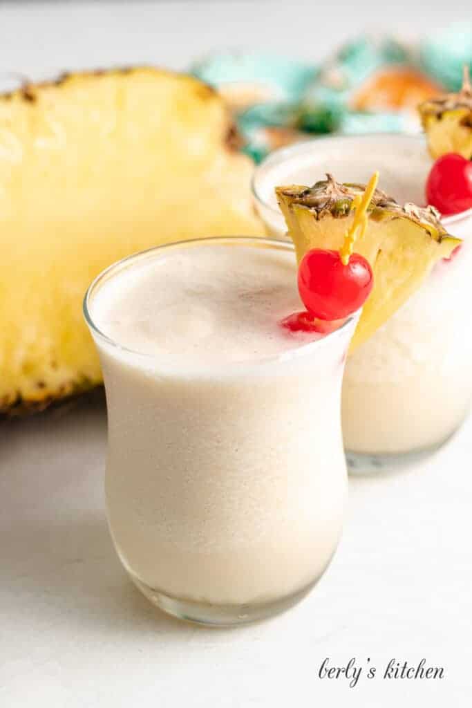Two cocktails garnished with cherries and sliced pineapple.