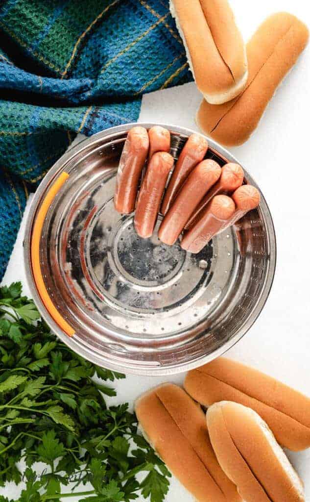 Uncooked hot dogs in a steamer basket.