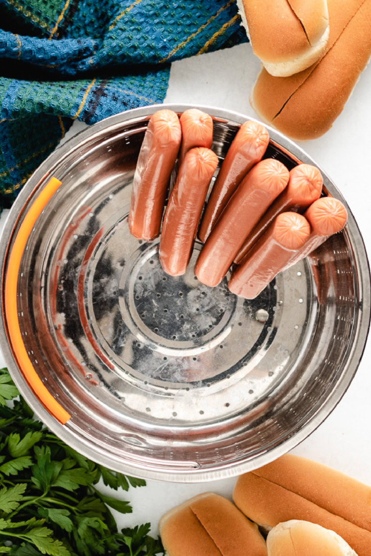 Uncooked hot dogs in a steamer basket.