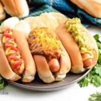 Three hot dogs topped with chili, cheese, and other condiments.