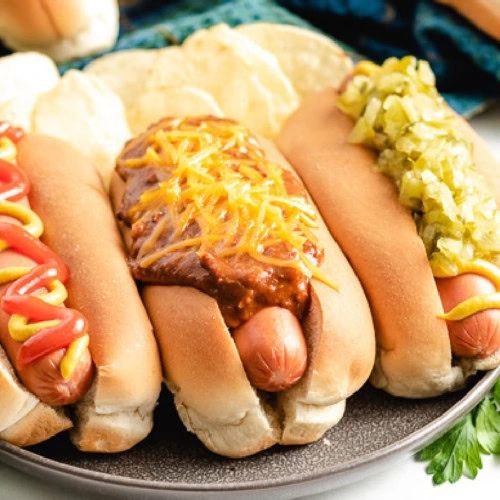 Three hot dogs topped with chili, cheese, and other condiments.