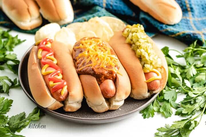 Three hot dogs topped with chili, cheese, and other condiments.