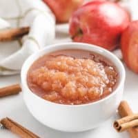 The applesauce surrounded by fresh cinnamon sticks and apples.