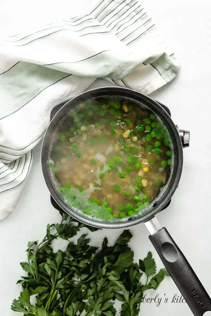 Macaroni, peas, and corn boiling together in a saucepan.