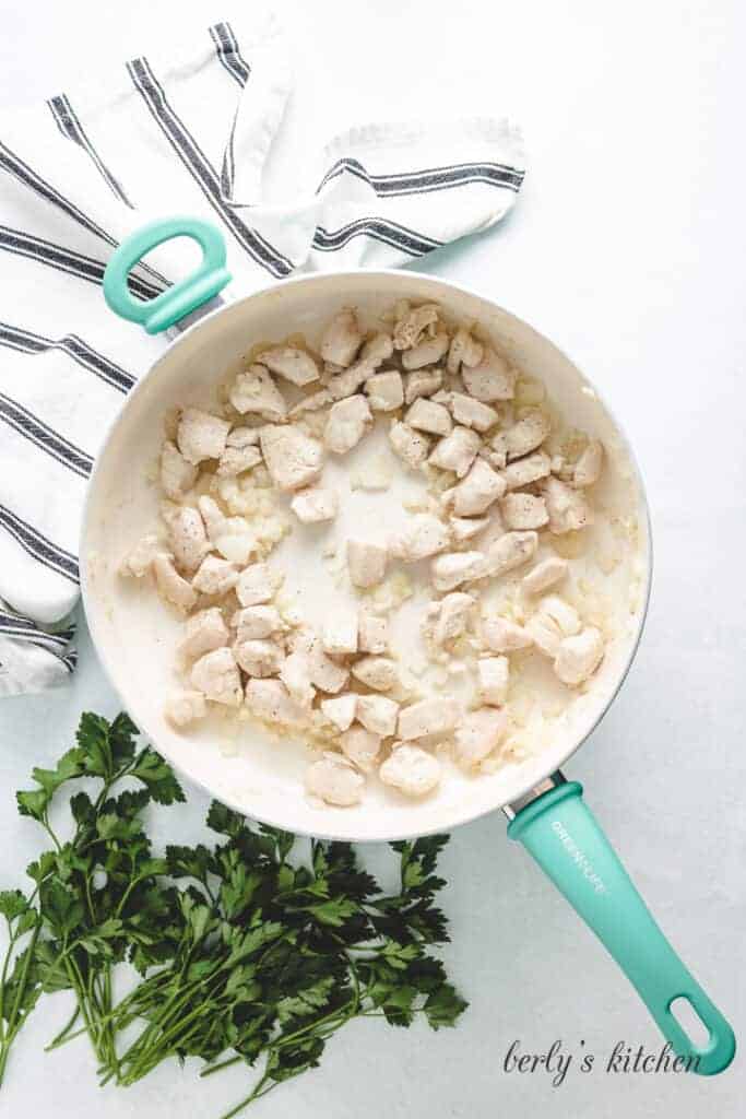 Diced chicken breast cooking in a pan.
