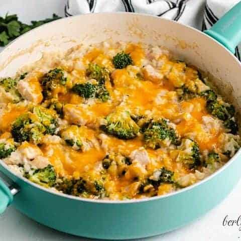 Cheesy Chicken Broccoli Rice Casserole A blue skillet filled with cheesy chicken rice and broccoli.