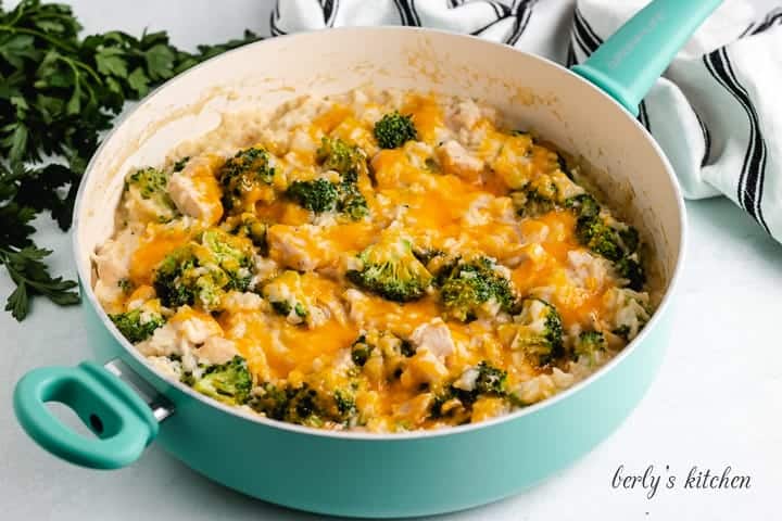 A blue skillet filled with cheesy chicken rice and broccoli.