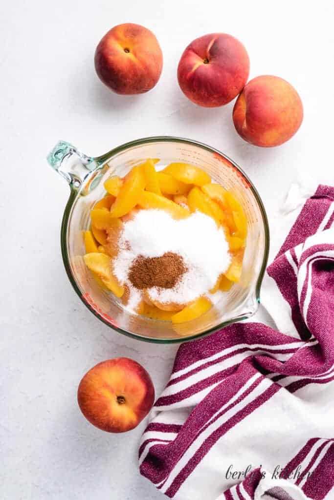 Peaches, cinnamon, and other ingredients in a large measuring cup.