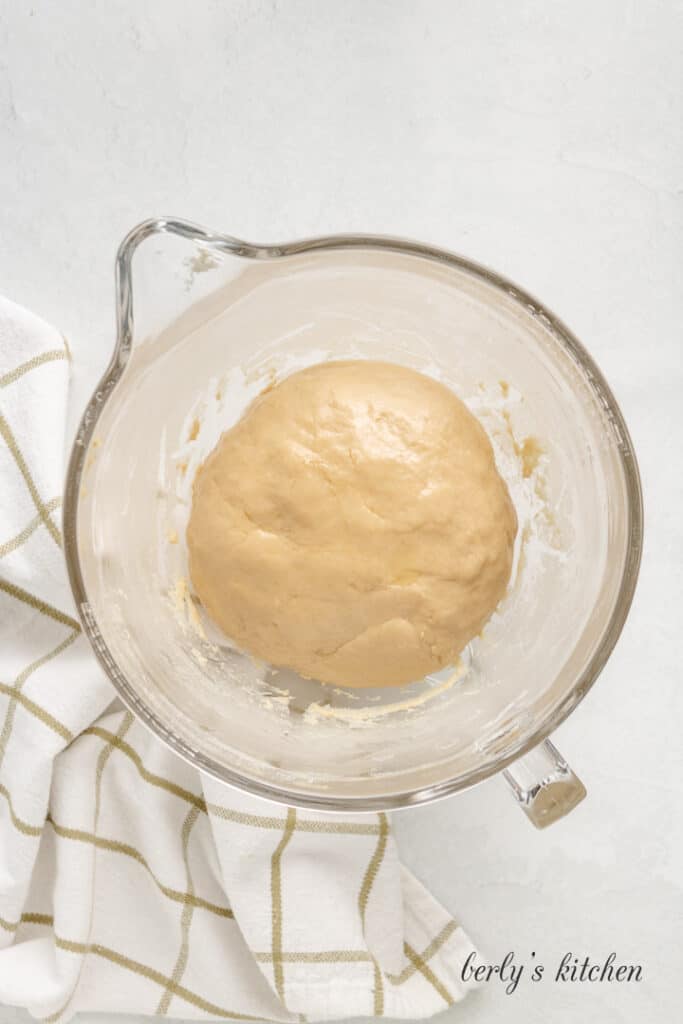 Mixed dough rising in a glass mixing bowl.