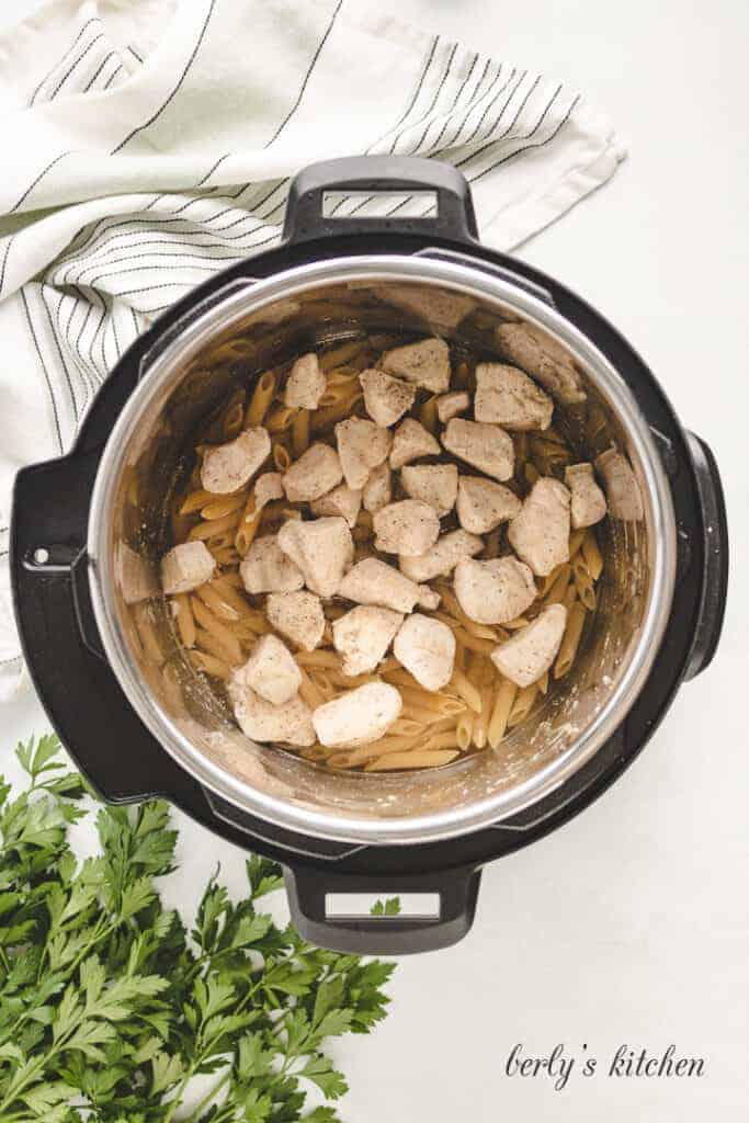 Chicken on top of noodles in a pressure cooker.