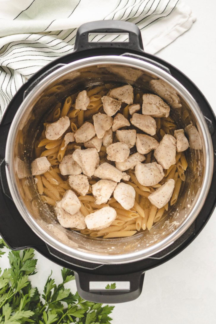 Chicken on top of noodles in a pressure cooker.