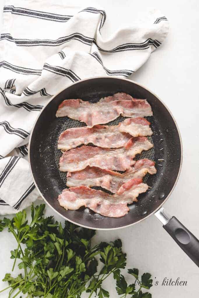 Five slices of bacon cooking in a skillet.