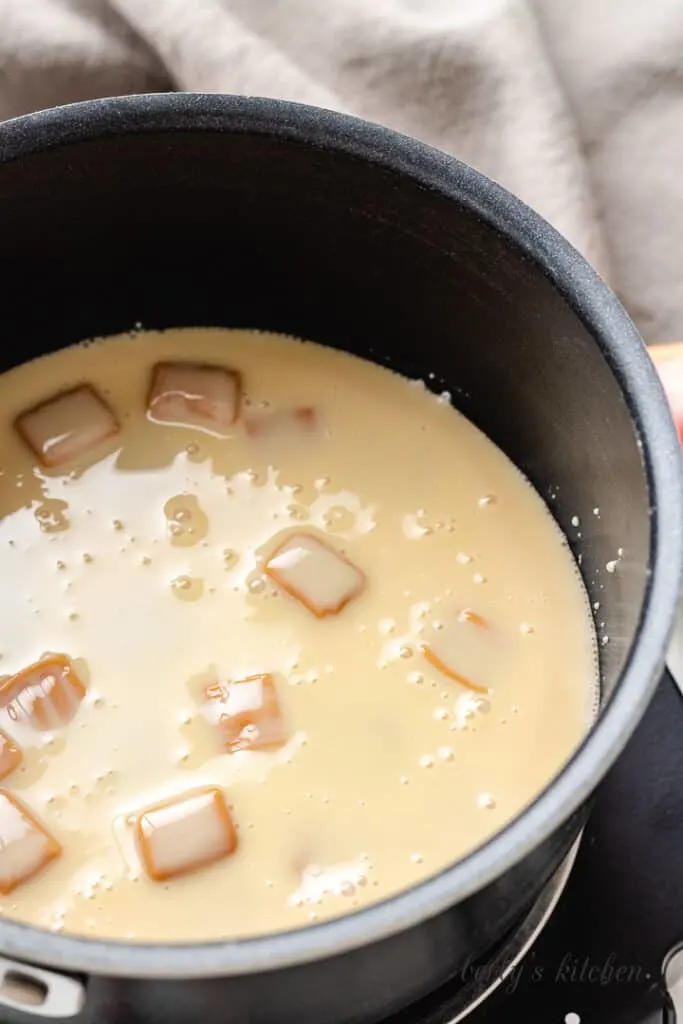 Caramel squares and sweetened condensed milk in a pan.