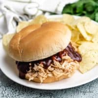 Slow cooker BBQ chicken on a bun with chips.
