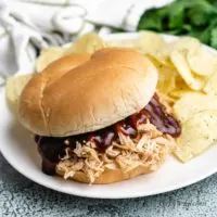 Slow cooker BBQ chicken on a bun with chips.