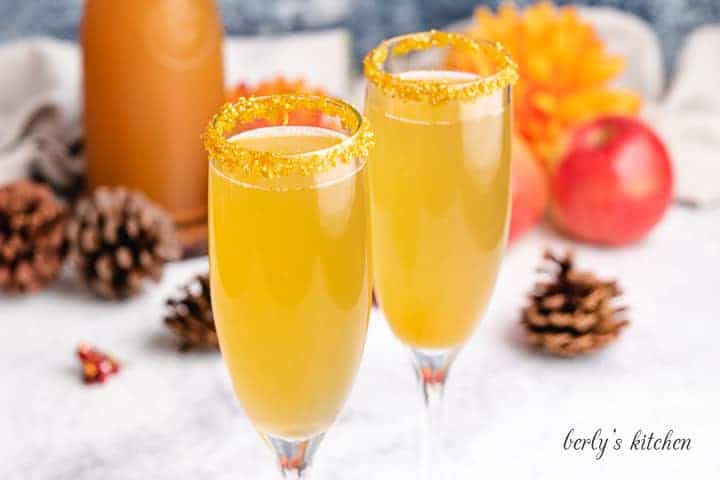 Apple cider mimosas in champagne glasses rimmed with golden sugar.